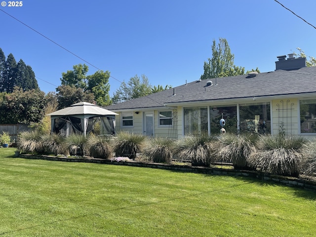 back of property featuring a gazebo, a lawn, a chimney, and a shingled roof