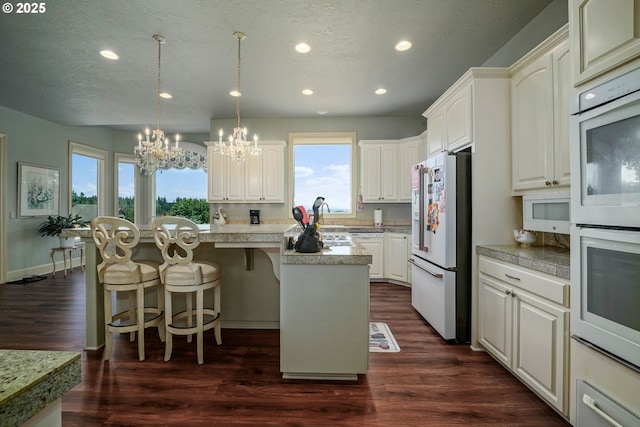 7947 Lavender Ln, Turner, OR 97392 - kitchen featuring white appliances, a chandelier, recessed lighting, a breakfast bar area, and dark wood finished floors