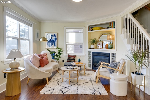 living room with crown molding, dark hardwood / wood-style flooring, a tiled fireplace, and built in features