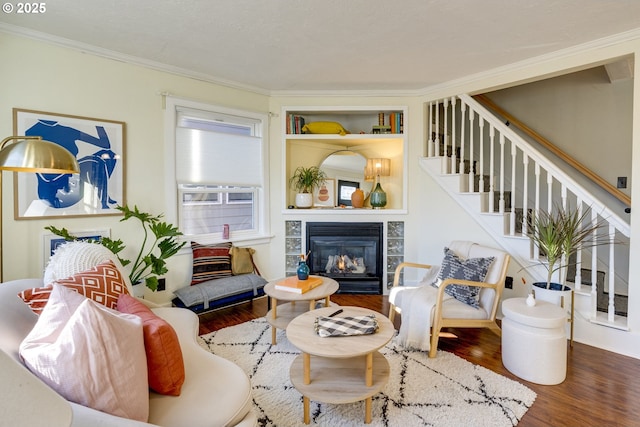 living room with crown molding, a tiled fireplace, hardwood / wood-style floors, and built in features