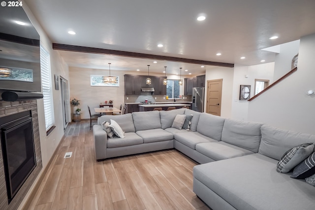 living room with light hardwood / wood-style flooring, beamed ceiling, and a stone fireplace