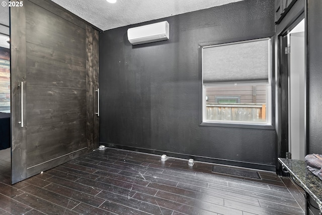 empty room with a textured wall, a textured ceiling, a wall unit AC, and dark wood-style flooring