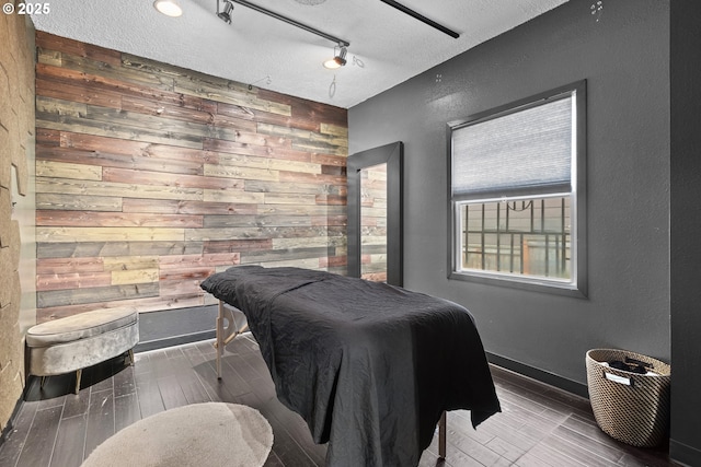 bedroom with track lighting, a textured ceiling, wood walls, baseboards, and wood tiled floor