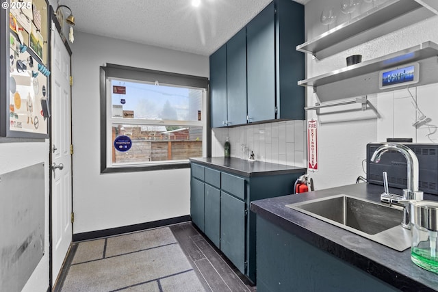 kitchen featuring a sink, a textured ceiling, dark countertops, blue cabinets, and tasteful backsplash