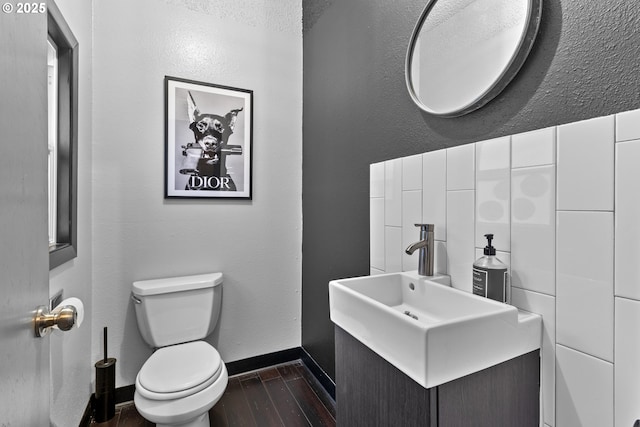 half bathroom featuring toilet, wood finished floors, baseboards, vanity, and a textured wall