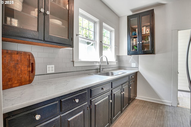 kitchen featuring baseboards, glass insert cabinets, a sink, and tasteful backsplash