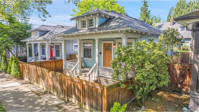 bungalow-style home featuring a porch, fence, and a shingled roof