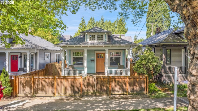 bungalow-style house featuring a porch, a shingled roof, and a fenced front yard