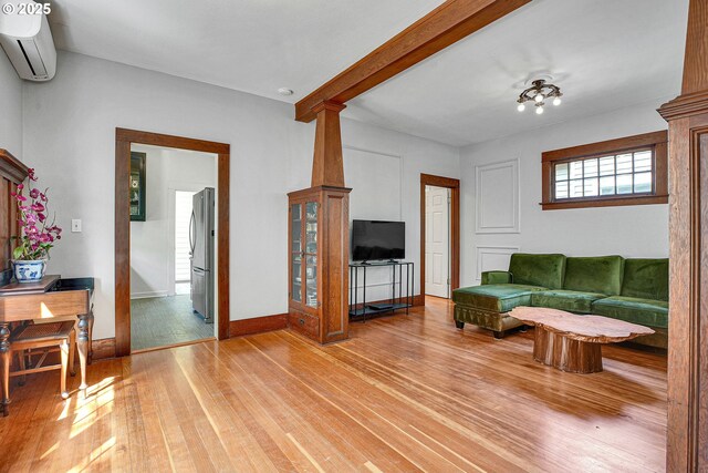 living area featuring baseboards, a wall unit AC, and light wood finished floors