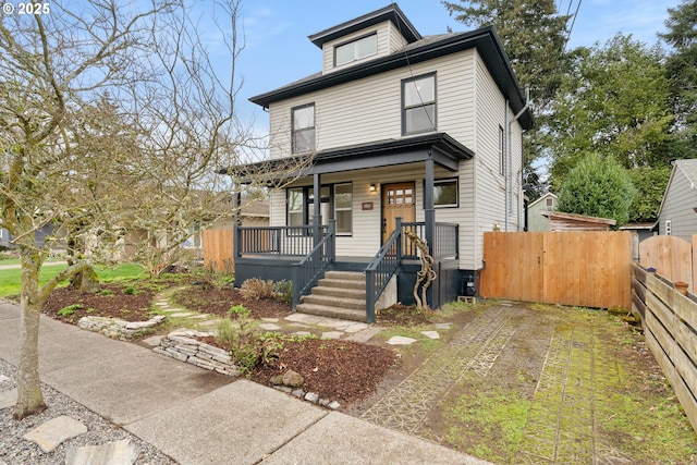 american foursquare style home featuring a porch, fence, and driveway