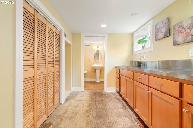 kitchen with a sink, stainless steel countertops, baseboards, and recessed lighting