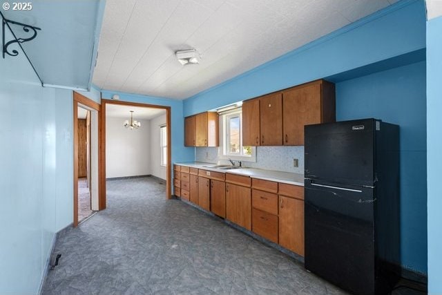 kitchen featuring freestanding refrigerator, a chandelier, brown cabinets, light countertops, and tile patterned floors
