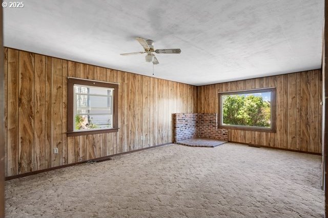 carpeted empty room with a ceiling fan and wood walls