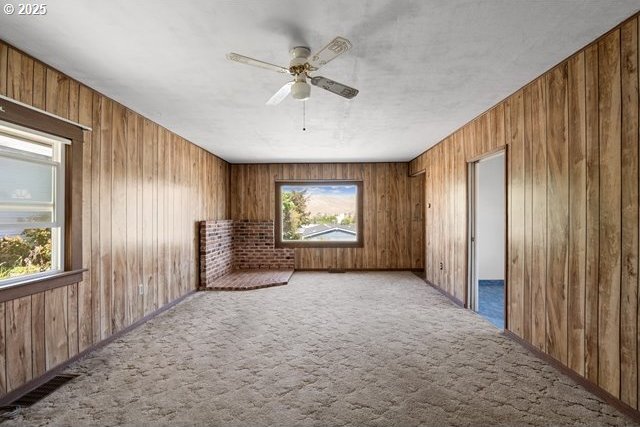 spare room featuring wood walls, a ceiling fan, and carpet flooring