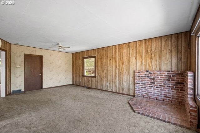 unfurnished living room featuring ceiling fan, wood walls, and carpet flooring
