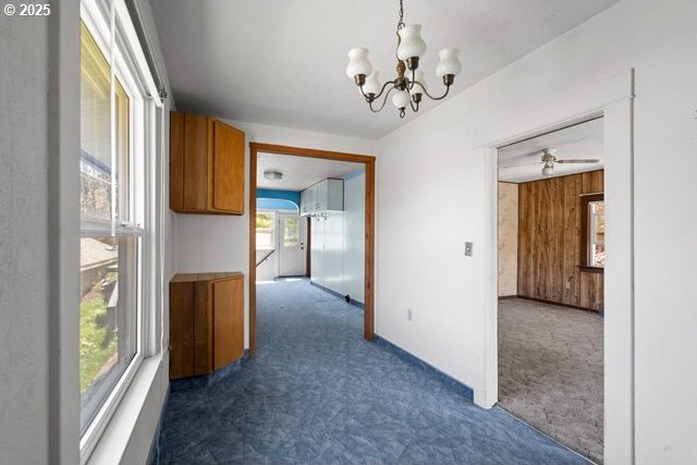 hall with a chandelier, dark carpet, and baseboards