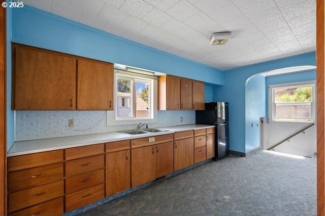 kitchen featuring a sink, freestanding refrigerator, light countertops, and brown cabinets