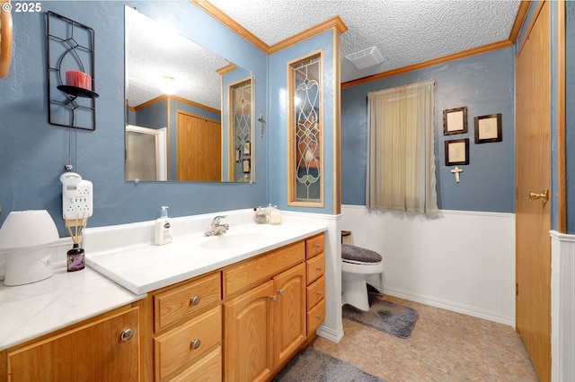 bathroom featuring wainscoting, vanity, toilet, a textured ceiling, and ornamental molding