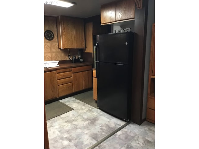 kitchen with freestanding refrigerator, light floors, brown cabinets, and dark countertops