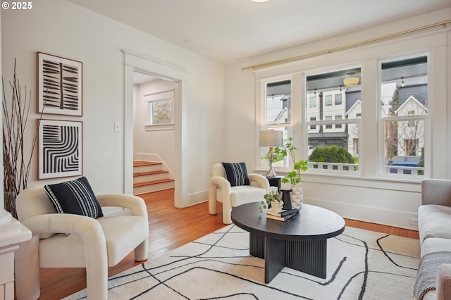 living room featuring baseboards, light wood-style flooring, and stairway