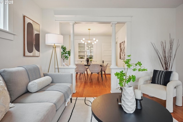 living area with light wood-style flooring, decorative columns, and a chandelier