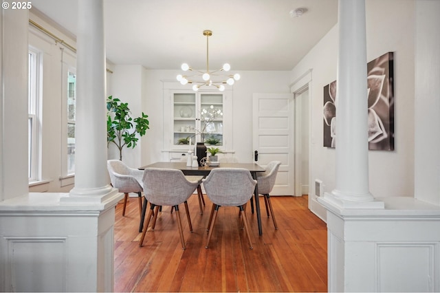 dining space with ornate columns, light wood-style floors, a notable chandelier, and visible vents