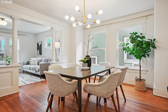 dining area with an inviting chandelier, decorative columns, and light wood-style flooring