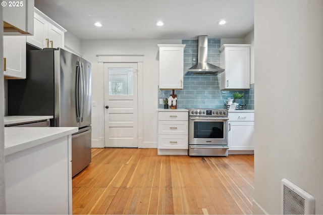 4131 NE Cleveland Ave, Portland, OR 97211 - kitchen with stainless steel appliances, wall chimney exhaust hood, white cabinets, light countertops, and light wood-type flooring