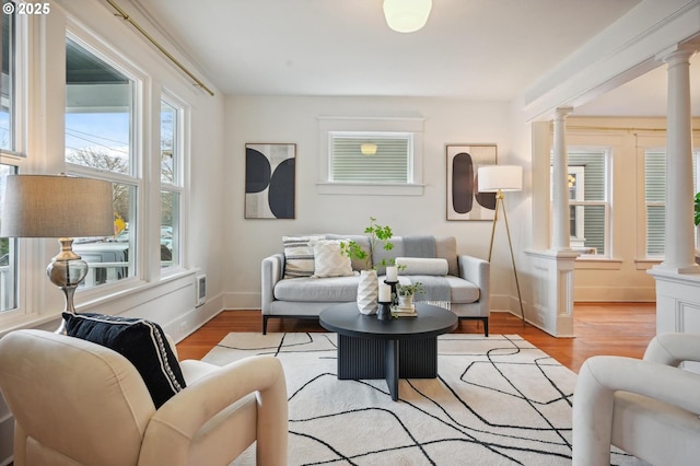 living area featuring ornate columns, baseboards, and wood finished floors