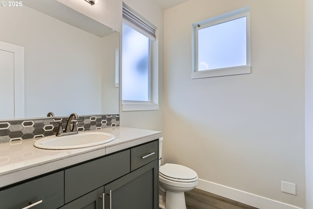 bathroom with toilet, wood finished floors, vanity, baseboards, and backsplash