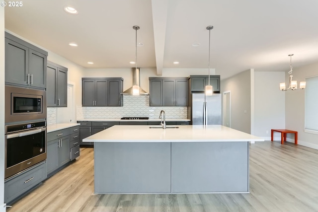 kitchen featuring wall chimney range hood, light wood-style floors, stainless steel appliances, and a sink