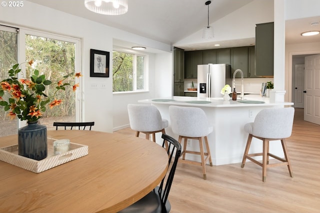 kitchen with a breakfast bar, light countertops, vaulted ceiling, light wood-style flooring, and stainless steel fridge