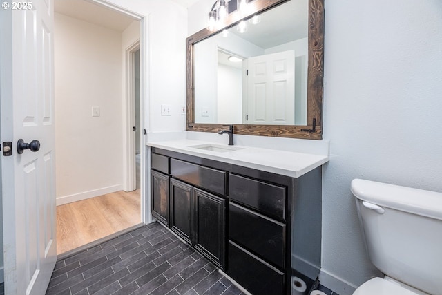 bathroom with vanity, toilet, wood finished floors, and baseboards