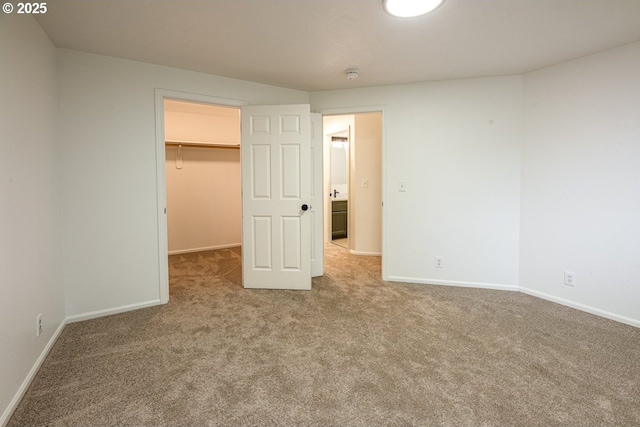 unfurnished bedroom featuring a closet, carpet flooring, a walk in closet, and baseboards