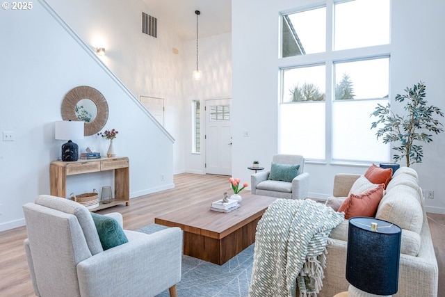 living area with visible vents, wood finished floors, stairway, baseboards, and a towering ceiling