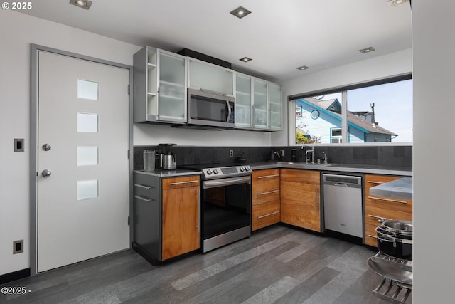3109 NW Neptune Ave, Lincoln City, OR 97367 - kitchen with stainless steel appliances, dark wood-style floors, glass insert cabinets, brown cabinetry, and dark countertops