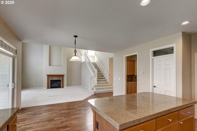 13605 NW Hogan St, Portland, OR 97229 - kitchen with tile countertops, a textured ceiling, light wood finished floors, a fireplace with flush hearth, and decorative light fixtures