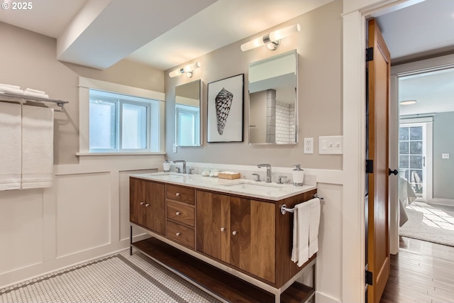 bathroom featuring double vanity, a sink, a wealth of natural light, and a decorative wall