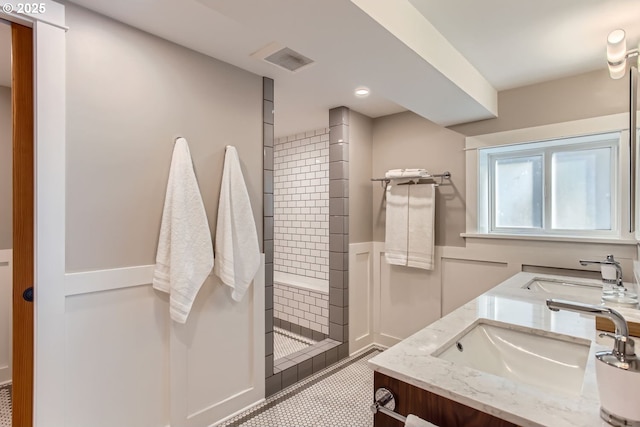 full bathroom featuring a tile shower, wainscoting, a sink, and a decorative wall