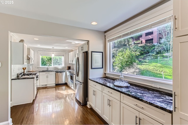 kitchen with dark wood-style floors, stainless steel appliances, decorative backsplash, a sink, and dark stone counters