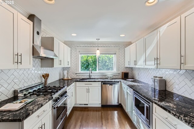 kitchen with stainless steel appliances, wall chimney exhaust hood, a sink, and white cabinets