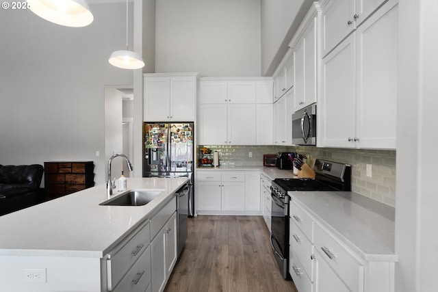 kitchen with appliances with stainless steel finishes, wood finished floors, a sink, light countertops, and backsplash