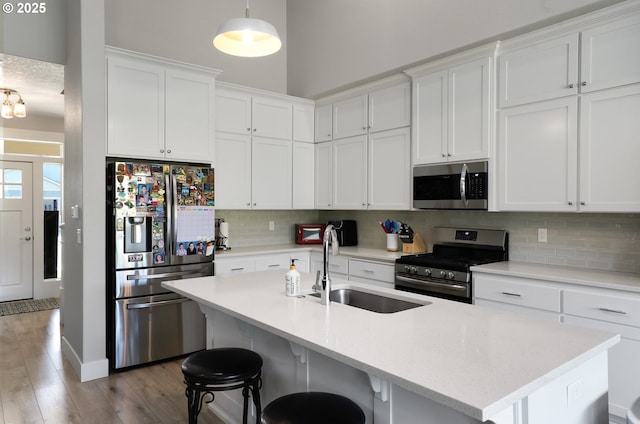 kitchen with light wood finished floors, stainless steel appliances, decorative backsplash, white cabinets, and a sink