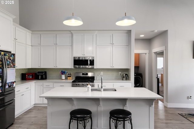 kitchen featuring stainless steel appliances, a sink, white cabinets, light countertops, and decorative backsplash