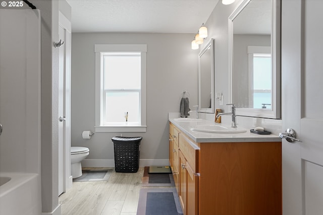 full bathroom with toilet, a sink, wood finished floors, a bath, and double vanity