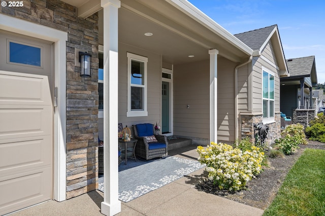 entrance to property with a porch, stone siding, roof with shingles, and an attached garage