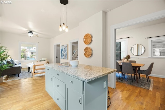 kitchen with a center island, hanging light fixtures, light wood-type flooring, ceiling fan, and a breakfast bar area