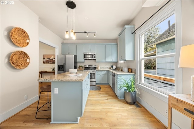 kitchen with decorative light fixtures, light hardwood / wood-style floors, stainless steel appliances, and a kitchen island