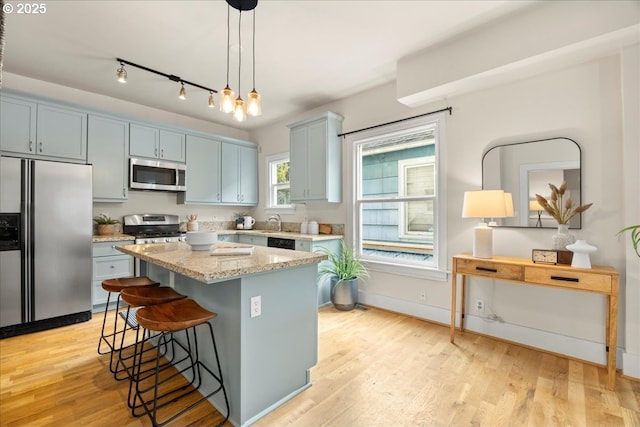 kitchen with pendant lighting, a center island, light wood-type flooring, light stone countertops, and appliances with stainless steel finishes