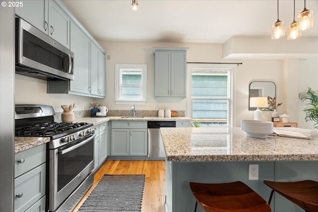 kitchen with a kitchen bar, hanging light fixtures, light wood-type flooring, stainless steel appliances, and light stone counters